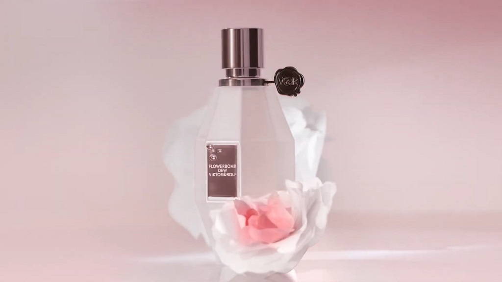 Bočica parfema Viktor & Rolf Flowerbomb postavljena među nežnim belim i roze laticama, na pastelno ružičastoj pozadini