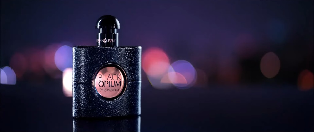 Bočica parfema Yves Saint Laurent Black Opium na tamnoj pozadini sa svetlima grada u defokusu, odiše misterioznim luksuzom